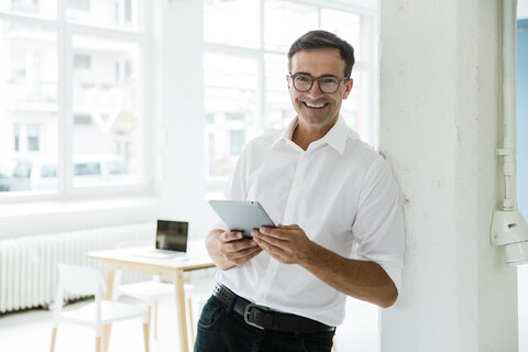 Porträt eines glücklichen Geschäftsmannes mit Tablet in einem hellen Büro, lizenzfreies Stockfoto