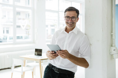 Porträt eines glücklichen Geschäftsmannes mit Tablet in einem hellen Büro - MOEF01465