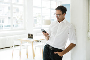 Geschäftsmann schaut auf Handy in hellem Büro - MOEF01466