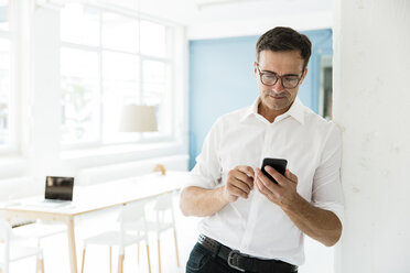 Geschäftsmann schaut auf Handy in hellem Büro - MOEF01467