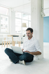 Geschäftsmann sitzt auf dem Boden im Büro und benutzt einen Laptop - MOEF01479