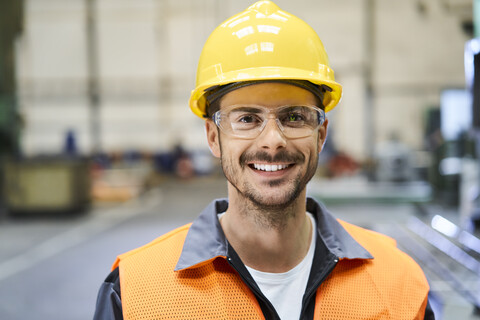 Porträt eines lächelnden Mannes in Arbeitsschutzkleidung in einer Fabrik, lizenzfreies Stockfoto