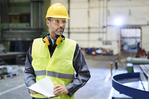 Mann in Arbeitsschutzkleidung sieht sich in einer Fabrik um, lizenzfreies Stockfoto