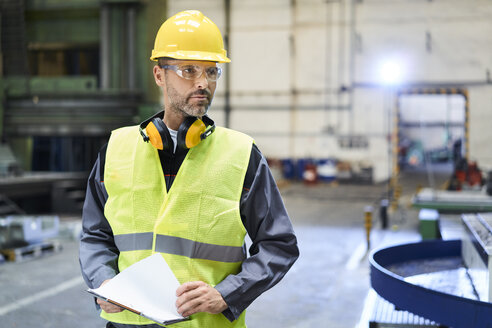 Mann in Arbeitsschutzkleidung sieht sich in einer Fabrik um - BSZF00588