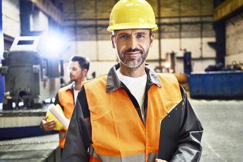 Porträt eines lächelnden Mannes in Arbeitsschutzkleidung in einer Fabrik, lizenzfreies Stockfoto
