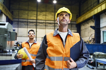 Zwei Männer in Arbeitsschutzkleidung sehen sich in einer Fabrik um - BSZF00595