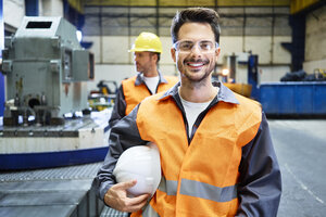 Porträt eines lächelnden Mannes in Arbeitsschutzkleidung in einer Fabrik - BSZF00597