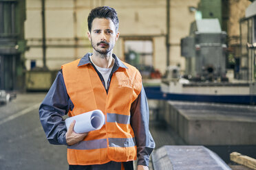 Porträt eines ernsten Mannes, der Blaupausen in einer Fabrik hält - BSZF00608