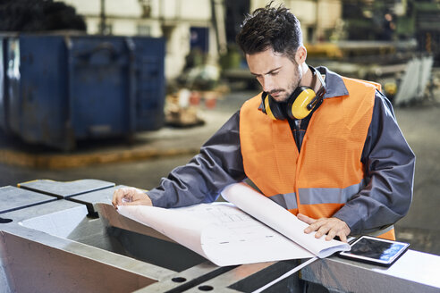 Ein Mann in Arbeitsschutzkleidung betrachtet einen Bauplan in einer Fabrik - BSZF00612