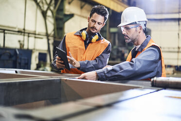 Zwei Männer in Arbeitsschutzkleidung bei der Arbeit mit einem Tablet in einer Fabrik - BSZF00614