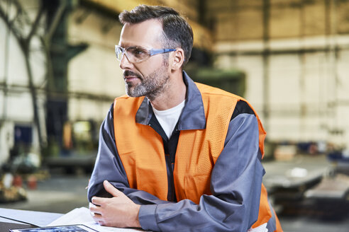 Porträt eines Mannes in einer Fabrik, der eine Schutzbrille trägt und sich umschaut - BSZF00615