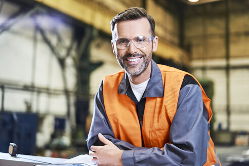 Porträt eines lächelnden Mannes in einer Fabrik mit Schutzbrille - BSZF00616