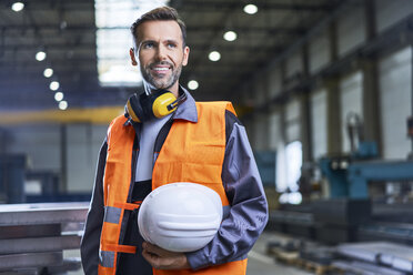 Porträt eines lächelnden Mannes in Arbeitsschutzkleidung in einer Fabrik - BSZF00621