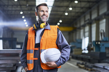 Porträt eines lächelnden Mannes in Arbeitsschutzkleidung in einer Fabrik - BSZF00622