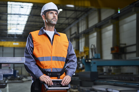 Porträt eines Mannes in einer Fabrik, der Maschinen mit einer Fernbedienungskonsole bedient, lizenzfreies Stockfoto