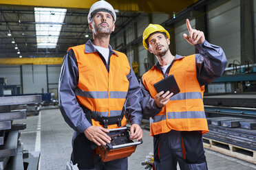 Two men in factory talking and operating machinery with remote console - BSZF00626