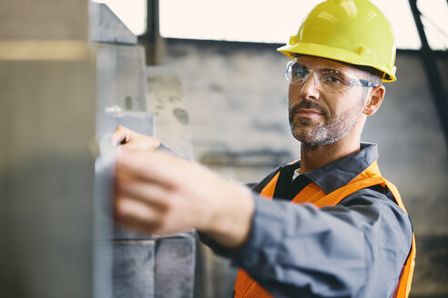 Porträt eines selbstbewussten Mannes in Arbeitsschutzkleidung bei der Arbeit in einer Fabrik - BSZF00630
