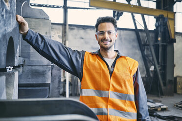 Porträt eines lächelnden Mannes in Arbeitsschutzkleidung in einer Fabrik - BSZF00633