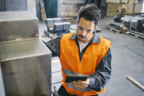 Mann mit Tablet und Arbeitsschutzkleidung bei der Arbeit in einer Fabrik - BSZF00635