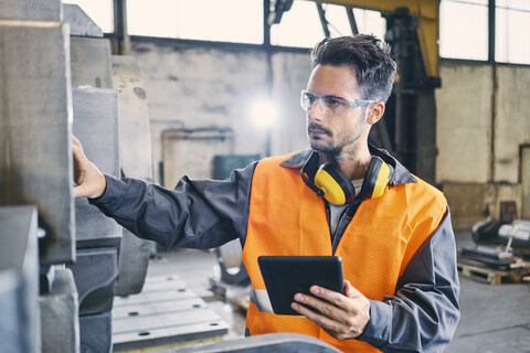 Mann mit Tablet und Arbeitsschutzkleidung bei der Arbeit in einer Fabrik, lizenzfreies Stockfoto