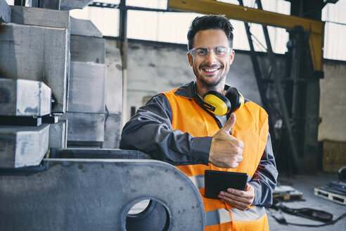 Porträt eines lächelnden Mannes in Arbeitsschutzkleidung, der den Daumen nach oben zeigt, in einer Fabrik - BSZF00639