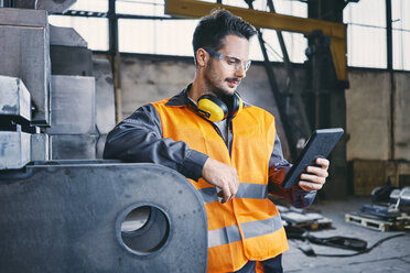 Mann mit Tablet und Arbeitsschutzkleidung bei der Arbeit in einer Fabrik - BSZF00640