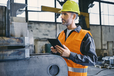 Mann mit Tablet und Arbeitsschutzkleidung bei der Arbeit in einer Fabrik - BSZF00641