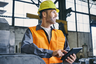 Lächelnder Mann mit Tablet in Arbeitsschutzkleidung in einer Fabrik - BSZF00643