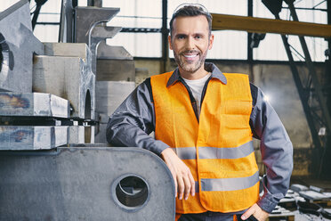 Porträt eines lächelnden Mannes in Arbeitsschutzkleidung in einer Fabrik - BSZF00646