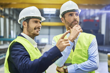 Zwei Manager in Arbeitsschutzkleidung im Gespräch in einer Fabrik - BSZF00648