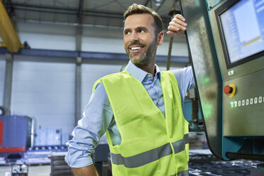 Lächelnder Ingenieur neben einem Computer in einer Fabrik - BSZF00654