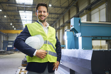 Portrait of smiling manager holding hard hat in factory - BSZF00656