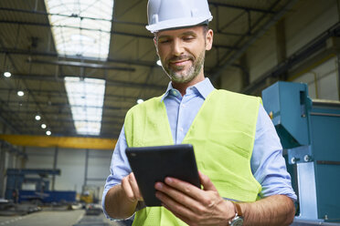 Selbstbewusster Mann mit Hemd und Sicherheitsweste, der in einer Fabrik ein Tablet benutzt - BSZF00659