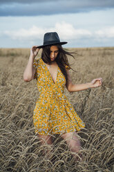 Junge Frau im Sommerkleid mit Blumenmuster und Hut tanzt im Maisfeld - VPIF00869