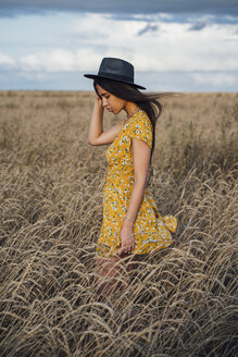 Junge Frau in Sommerkleid mit Blumenmuster und Hut in einem Maisfeld stehend - VPIF00870