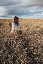 Rückenansicht einer jungen Frau, die in einem Maisfeld spazieren geht - VPIF00878