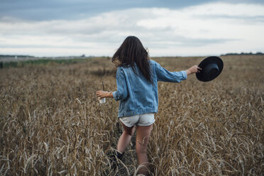 Back view of young woman with beverage and hat walking in corn field - VPIF00893