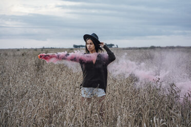 Portrait of young woman standing in a corn field with smoke torch - VPIF00897