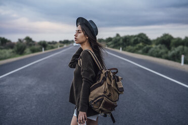 Portrait of hitchhiking young woman with backpack and beverage on lane - VPIF00905