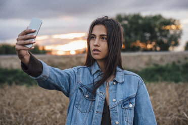 Porträt einer jungen Frau, die ein Selfie mit ihrem Smartphone in der Natur bei Sonnenuntergang macht - VPIF00909
