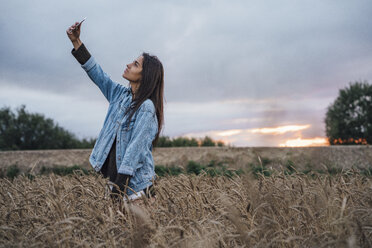 Junge Frau nimmt Selfie mit Smartphone in einem Maisfeld bei Sonnenuntergang - VPIF00910