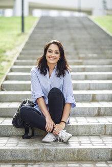 Porträt eines lächelnden Schülers, der auf einer Treppe im Freien sitzt - JSMF00448