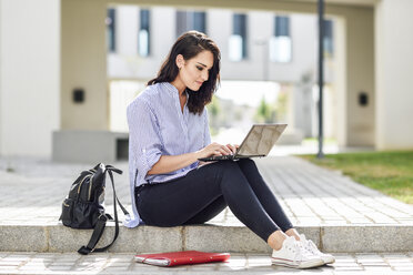 Zufriedener Student sitzt auf einer Treppe im Freien und arbeitet am Laptop - JSMF00454