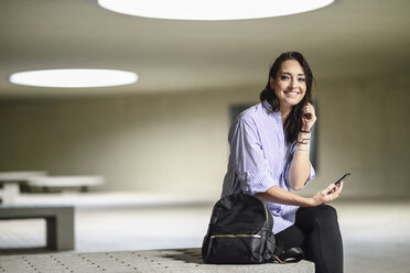 Portrait of smiling student with smartphone and backpack - JSMF00458