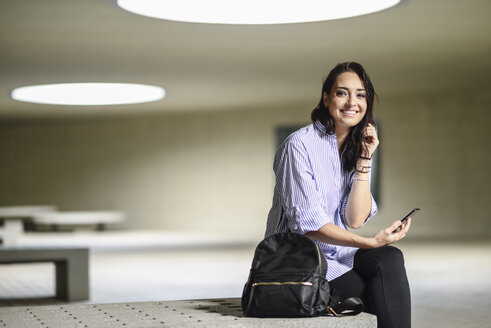 Porträt eines lächelnden Studenten mit Smartphone und Rucksack - JSMF00458