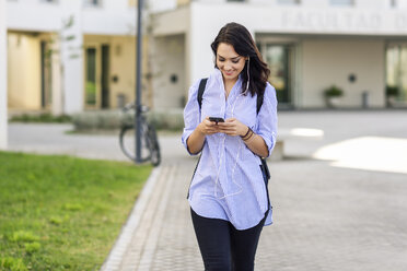 Portrait of smiling student using smartphone and earphones - JSMF00468