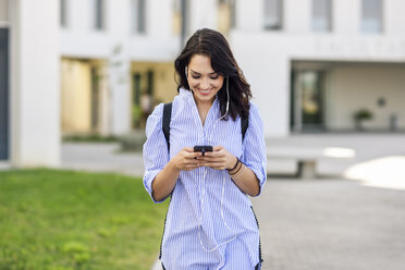 Portrait of smiling student using smartphone and earphones - JSMF00469