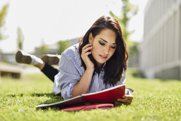 Porträt einer Studentin, die auf dem Rasen liegt und ihre Notizen liest - JSMF00476