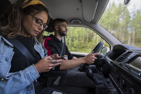 Young man driving car with woman checking cell phone - KKAF02076