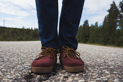 Finnland, Lappland, Füße eines Mannes, der auf einer leeren Landstraße steht, lizenzfreies Stockfoto